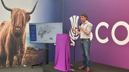 Gianluigi Rossi speaking on a stage. In the background there is a highland cow and screen with a map.